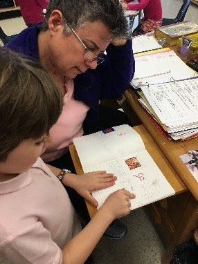 A volunteer assists a student reading a book